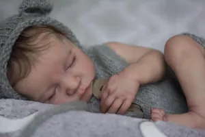 Close-up of lifelike newborn baby doll wearing gray bear ears knit hat and romper outfit