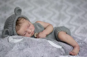 Detail of gray hand-knitted newborn doll outfit with bear ear hat and wooden buttons