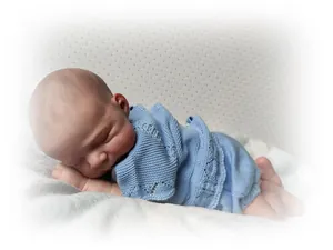 Close-up of 48cm reborn baby doll sleeping in a light blue hand-knitted newborn outfit