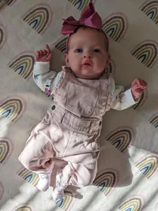 Detailed view of a 55cm lifelike reborn baby doll in pink overalls on a rainbow blanket