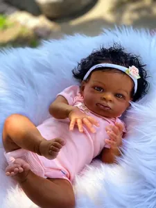 Primer plano de una muñeca reborn con piel oscura, pelo rizado y diadema rosa sobre piel blanca