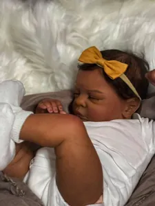 Detailed view of 49cm reborn baby doll Romy sleeping in white cotton bodysuit with yellow bow