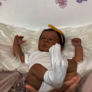 Realistic 49cm reborn baby doll with 3D deep skin tone in white cotton bodysuit and yellow headband