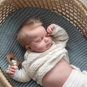 Lifelike 19-inch sleeping reborn baby doll in waffle knit sweater resting in woven basket