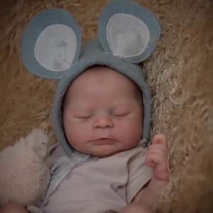 Realistic 49cm reborn baby doll with visible veins and blue mouse ear hat on plush background