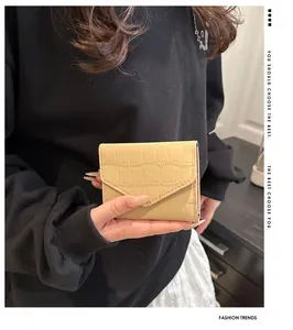 Detalle de la cartera beige con patrón de cocodrilo sostenida por la mano en casa
