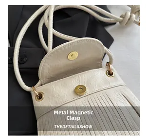 Macro detail of creamy faux suede crossbody bag featuring magnetic buckle and fringe