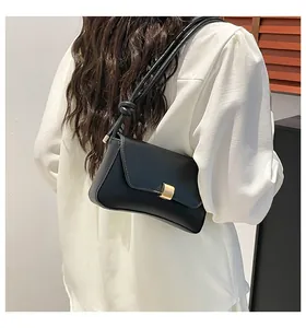 Detail of black leather bag with a gold buckle and knotted strap on a model shoulder
