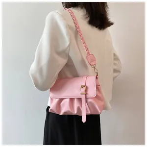 Détail du sac à bandoulière rose plissé avec sangle tressée et boucle dorée sur un blazer