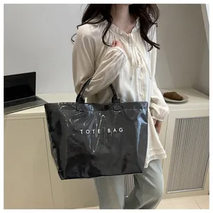 Detail einer schwarzen glänzenden PVC-Tasche mit TOTE BAG Aufdruck in einer Alltagsszene