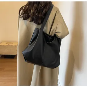 Detailed view of a black pebbled leather tote bag worn with a long beige coat