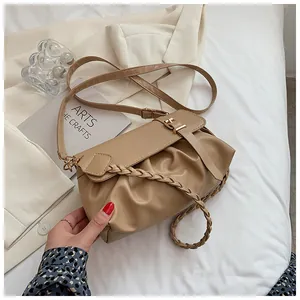 Détail du sac bandoulière plissé en cuir kaki avec poignée tressée sur lit blanc