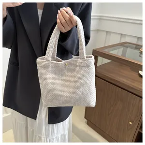 Close-up of cream woven tote bag featuring a textured pattern and gold metal buckle