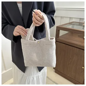 Detail of a woven cream tote bag showing thick texture and a gold metal fastener