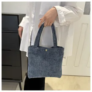 Detail of navy blue textured knit tote bag featuring a round golden metallic button closure