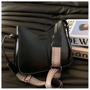 Close-up of black glossy leather shoulder bag with ethnic pattern wide strap and metal buckle