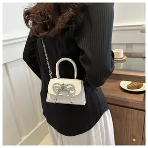Detail of white mini handbag featuring a sparkling rhinestone bow and silver chain