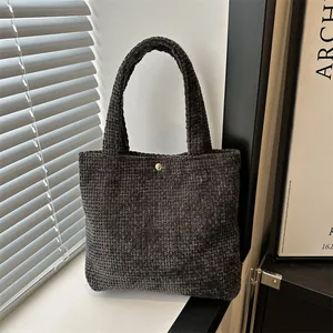 Minimalist dark grey woven knit tote bag with gold snap button in soft natural light