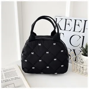 Detail of black quilted handbag with white bow embroidery and soft fabric handle