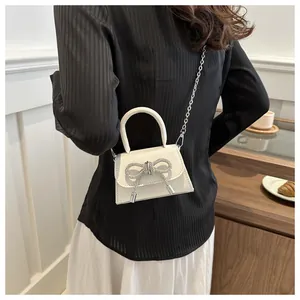 Detailed view of mini cream crossbody bag with sparkling rhinestone bow and chain strap