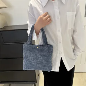 Blue woven tote bag with textured knit fabric and gold button closure for women