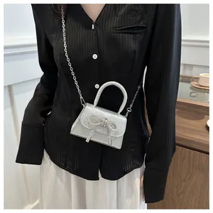 Detail of a silver sequined mini handbag with a rhinestone bow and metal chain strap
