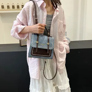 Sac à main rétro en denim bleu avec bandoulière en cuir brun porté par un mannequin