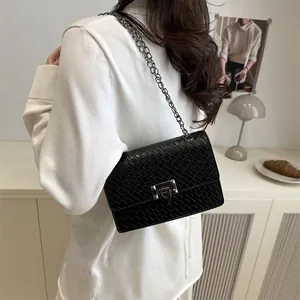 Bolso cuadrado negro con textura de cocodrilo, cadena plateada y cierre de giro elegante