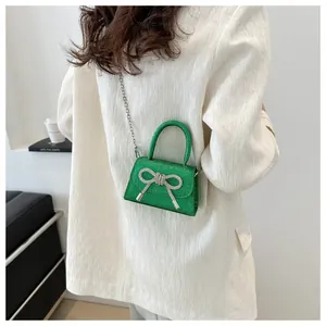 Green sequined mini crossbody bag with a rhinestone bow worn by a model in a suit