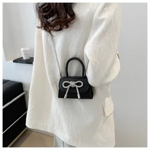 Detail of a mini black crossbody bag with a shiny silver rhinestone bow and metal chain
