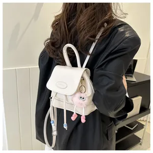 Detalle de una mini mochila de cuero blanco crema con un tierno colgante de peluche en modelo