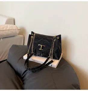 Detailaufnahme der glänzenden schwarzen Faltenledertasche mit goldener T-Metall-Schnalle
