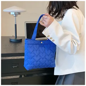 Detail of blue heart-quilted tote bag featuring metallic snap button and soft nylon texture
