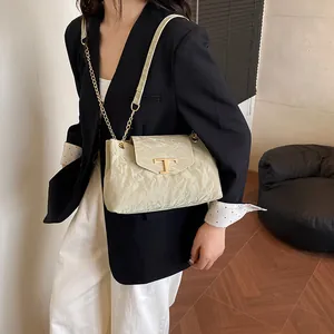 Elegante cremefarbene Tote Bag mit goldenem T-Logo und Kettengurt an einem Model