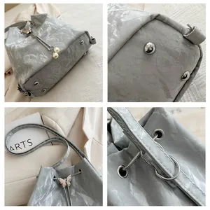 Vue détaillée du sac seau gris montrant la boucle papillon et les pieds métalliques de fond