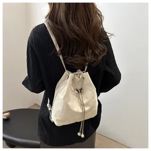 Sac à dos seau beige à cordon avec pendentif papillon en métal porté par un mannequin