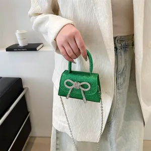 Mini green glitter chain handbag with silver rhinestone bow on white textured blazer