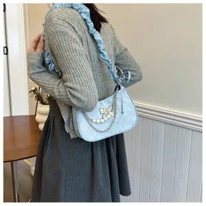 Detail of light blue crescent bag with metal bow, pearls, and ruffled cloud shoulder strap