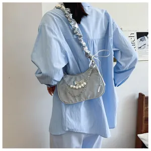 Detail of silver crescent bag featuring ruffled strap and pearl chain decoration