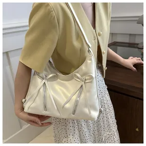 Détail du sac bandoulière crème avec nœuds décoratifs et détails de fermetures éclair