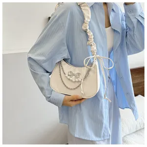 Close-up of creamy shoulder bag featuring a metallic bow, pearls, and ruffled cloud strap