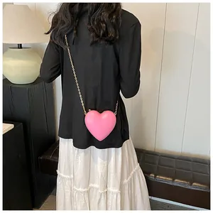 Sac à bandoulière rose en forme de cœur avec chaîne dorée porté par un mannequin