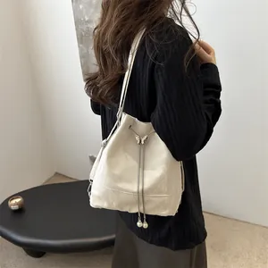 Sac seau en cuir crème avec papillon argenté et cordons en perles porté par un mannequin
