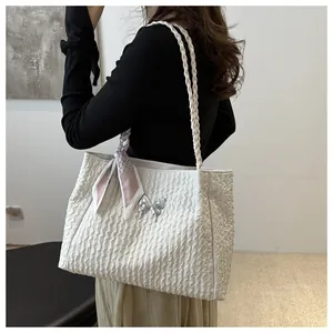 Detailed side view of white pleated tote bag with silk scarf and silver bow charm accessory