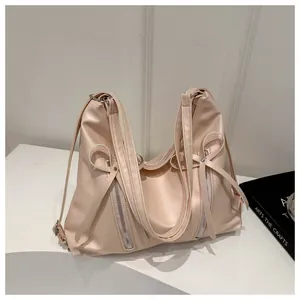 Detail of light pink hobo shoulder bag featuring decorative bows and vertical zippers