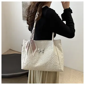Detail of cream pleated tote bag with silver butterfly charm and patterned silk scarf