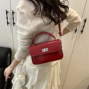 Glossy red square handbag with silver turn-lock clasp shown as crossbody on model