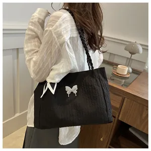 Detail of black pleated tote bag with silver butterfly charm and braided rope shoulder straps