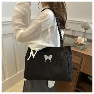 Close-up of pleated black tote bag with white butterfly charm and braided straps