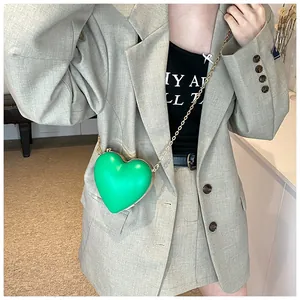Détail du sac à main cœur vert vif avec chaîne dorée porté sur une veste de blazer grise